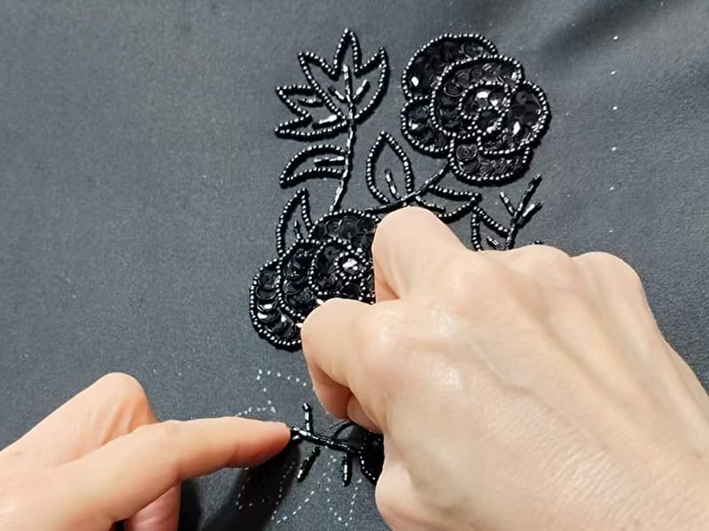 Skilled artisan hand-beading sequin rose embroidery on evening clutch fabric